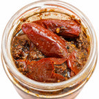 Handmade red chili pickle in glass jar with mustard oil, spices, and whole chilies, crafted by rural artisans.